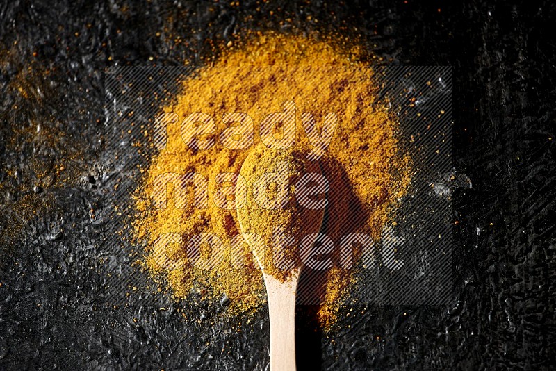 A wooden spoon full of turmeric powder on textured black background