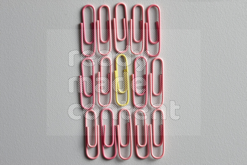 A bunch of pink paper clips with a different colored paper clip in the center on grey background