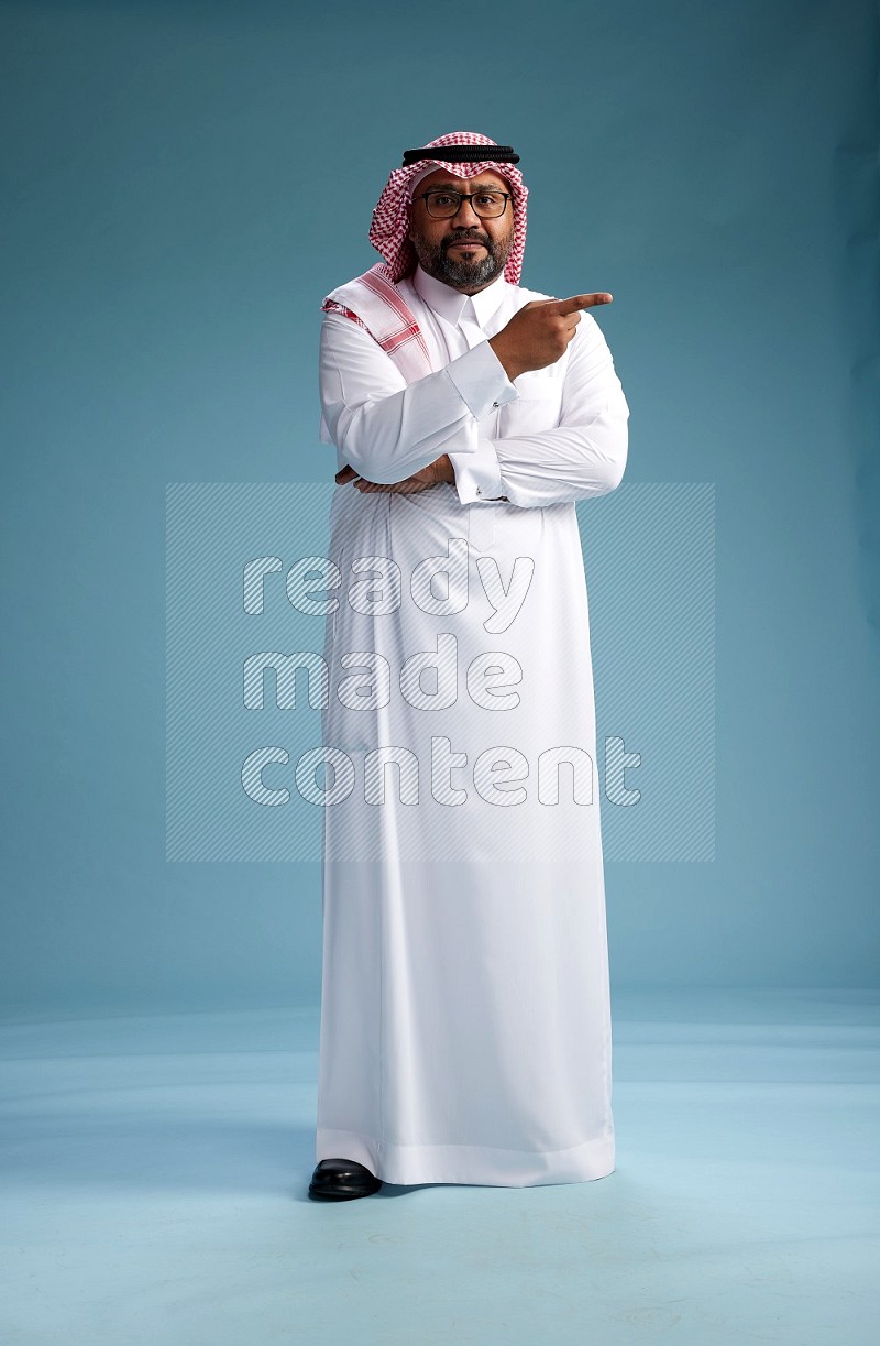 Saudi Man with shimag Standing Interacting with the camera on blue background