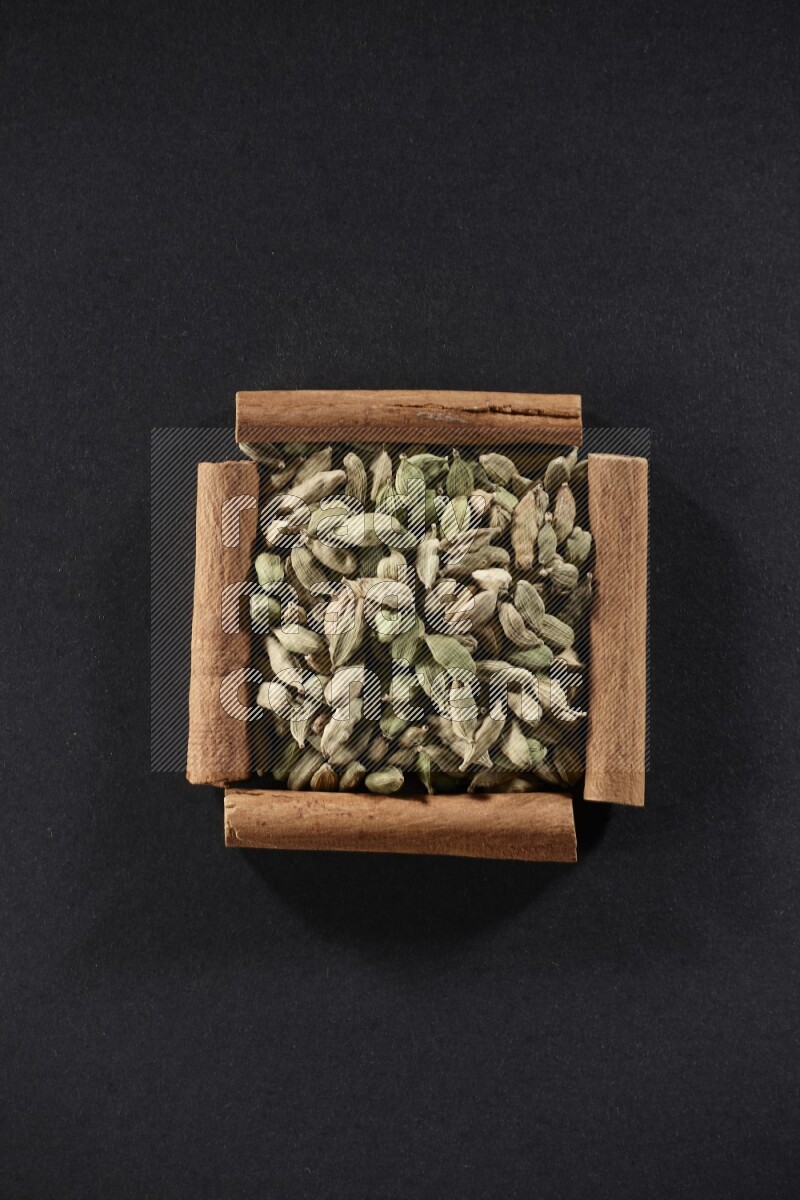 A single square of cinnamon sticks full of Cardamom on black flooring