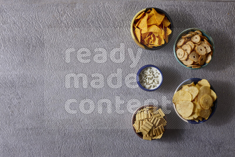 Assorted snacks in pottery bowls on grey background