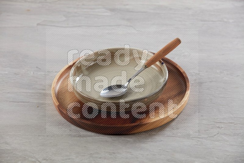 multi color pottery round dish on top of brown wood round plate and spoon, on grey textured countertop