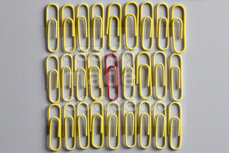 A bunch of yellow paper clips with a different colored paper clip in the center on grey background