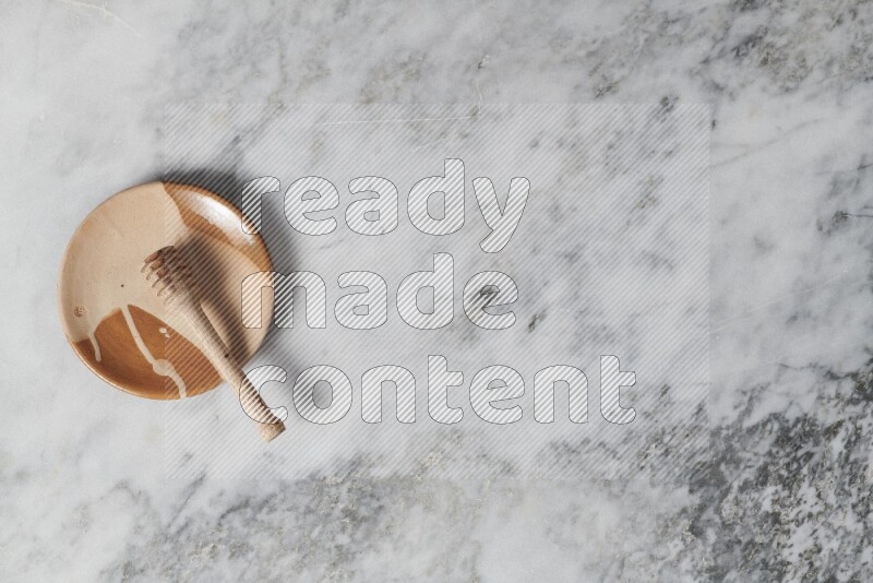 Multicolored pottery plate with wooden honey dipper in it on grey marble background
