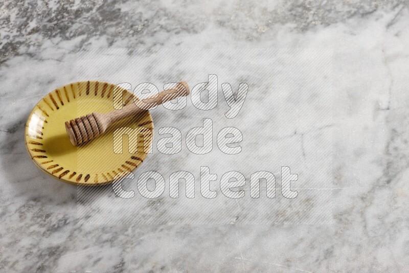Multicolored pottery plate with wooden honey dipper in it on grey marble background
