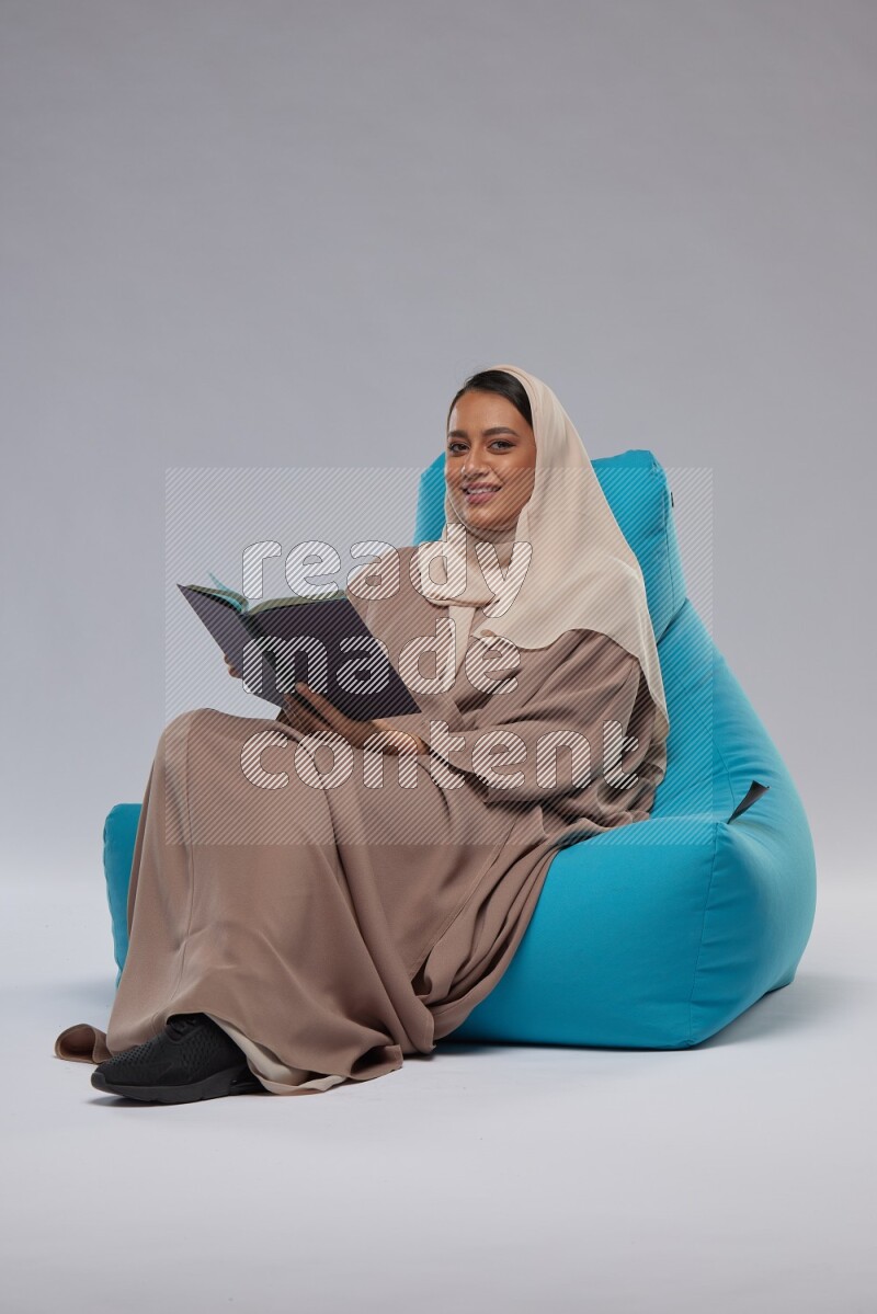 A woman sitting on a blue beanbag and reading a book