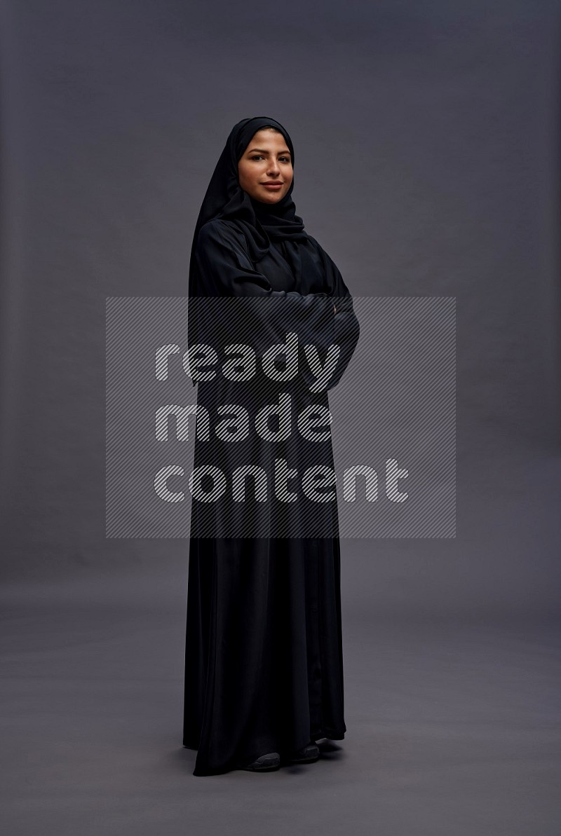 Saudi woman wearing Abaya standing with crossed arms on gray background