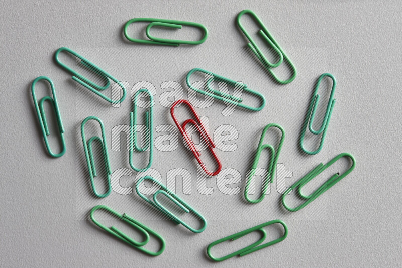 A red paperclip surrounded by bunch of green paperclips on grey background