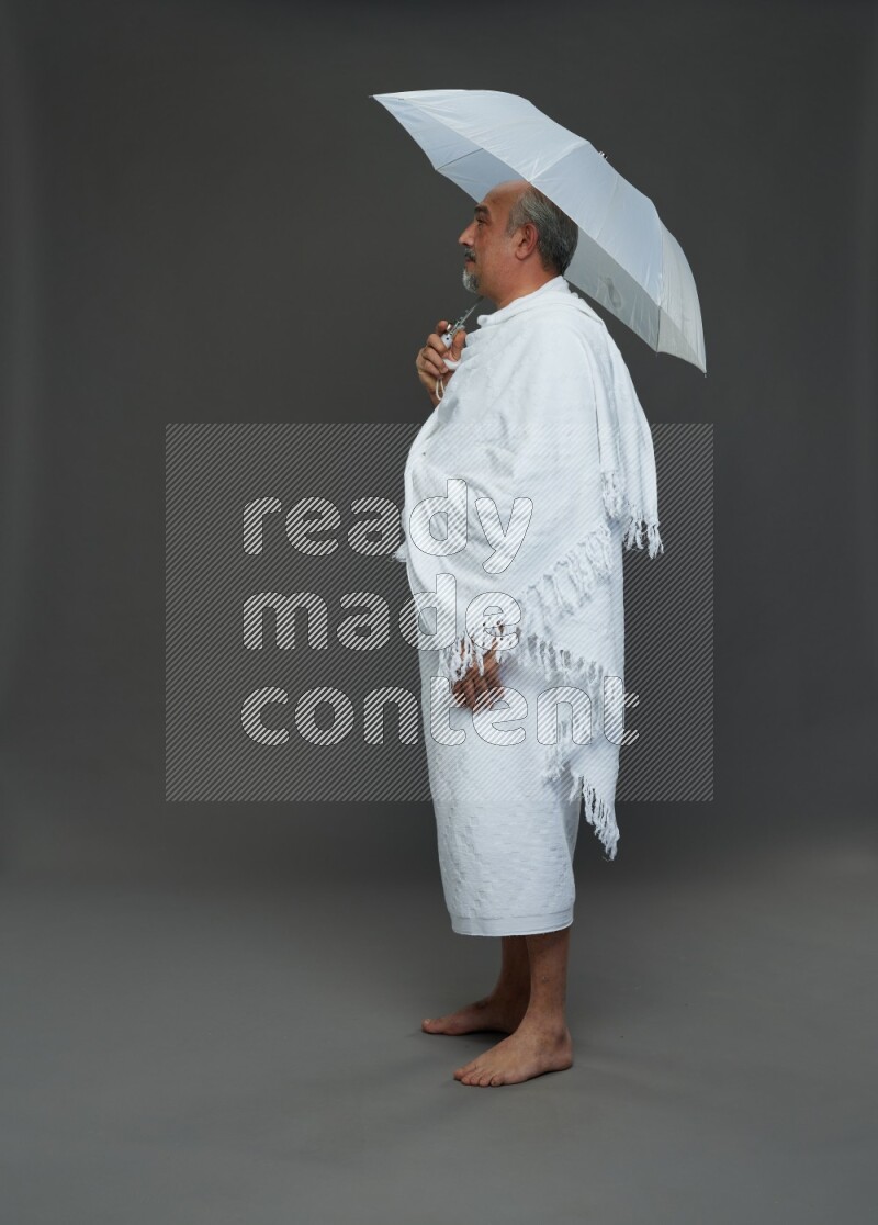 A man wearing Ehram Standing holding umbrella on gray background