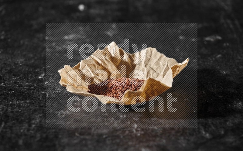 A crumpled piece of paper full of garden cress seeds on a textured black flooring