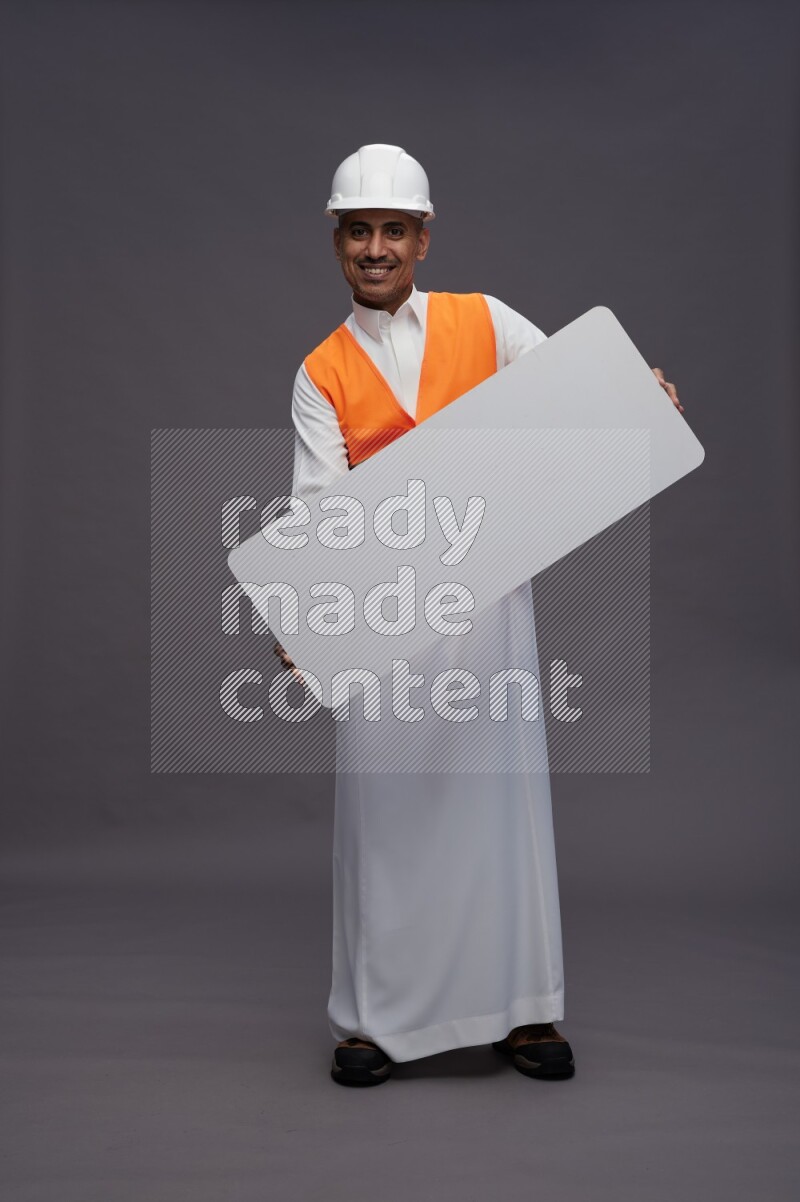 Saudi man wearing thob with engineer vest standing holding board on gray background