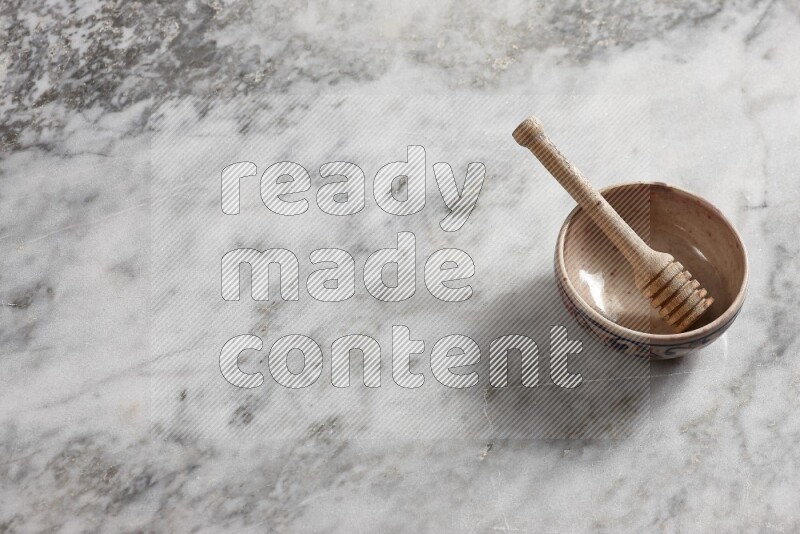 Decorative pottery bowl with wooden honey dipper in it on grey marble background