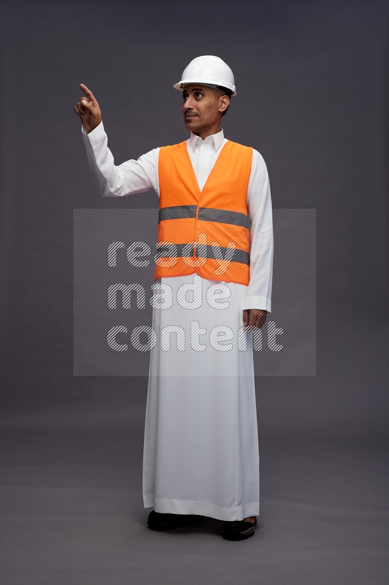 Saudi man wearing thob with engineer vest standing interacting with the camera on gray background