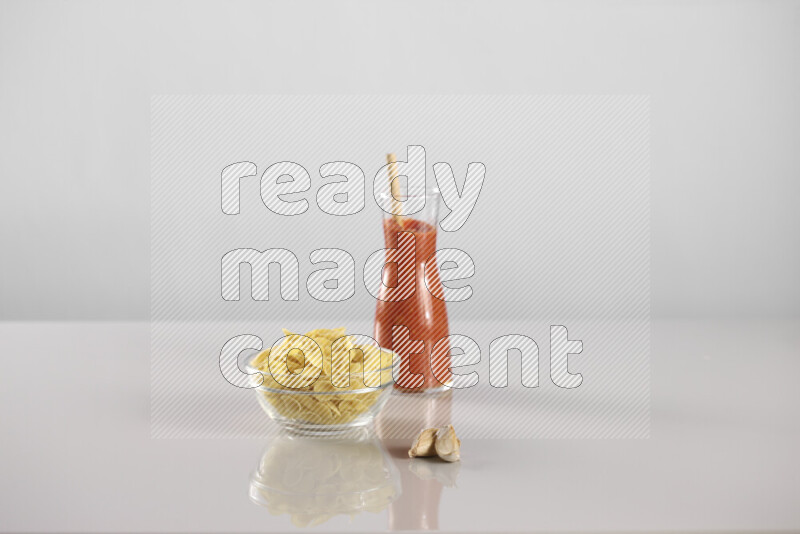 Raw pasta with tomatoe pasta with different ingredients such as cherry tomatoes, basil, garlic, bay laurel, cardamom, white pepper, black pepper, red chilis and wheat stalks on light grey background