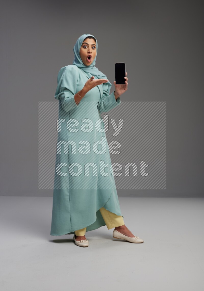 Saudi Woman wearing Abaya standing showing phone to camera on Gray background