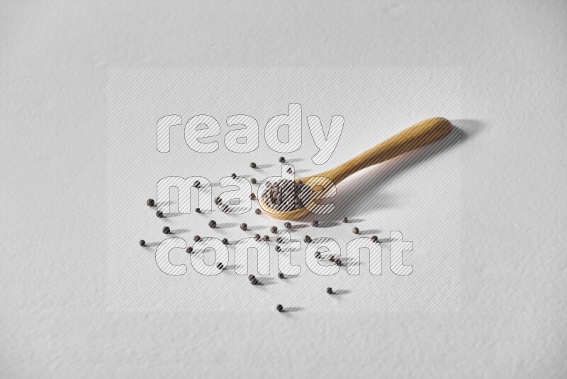 حبوب الفلفل الأسود في ملعقة خشبية علي خلفية بيضاء