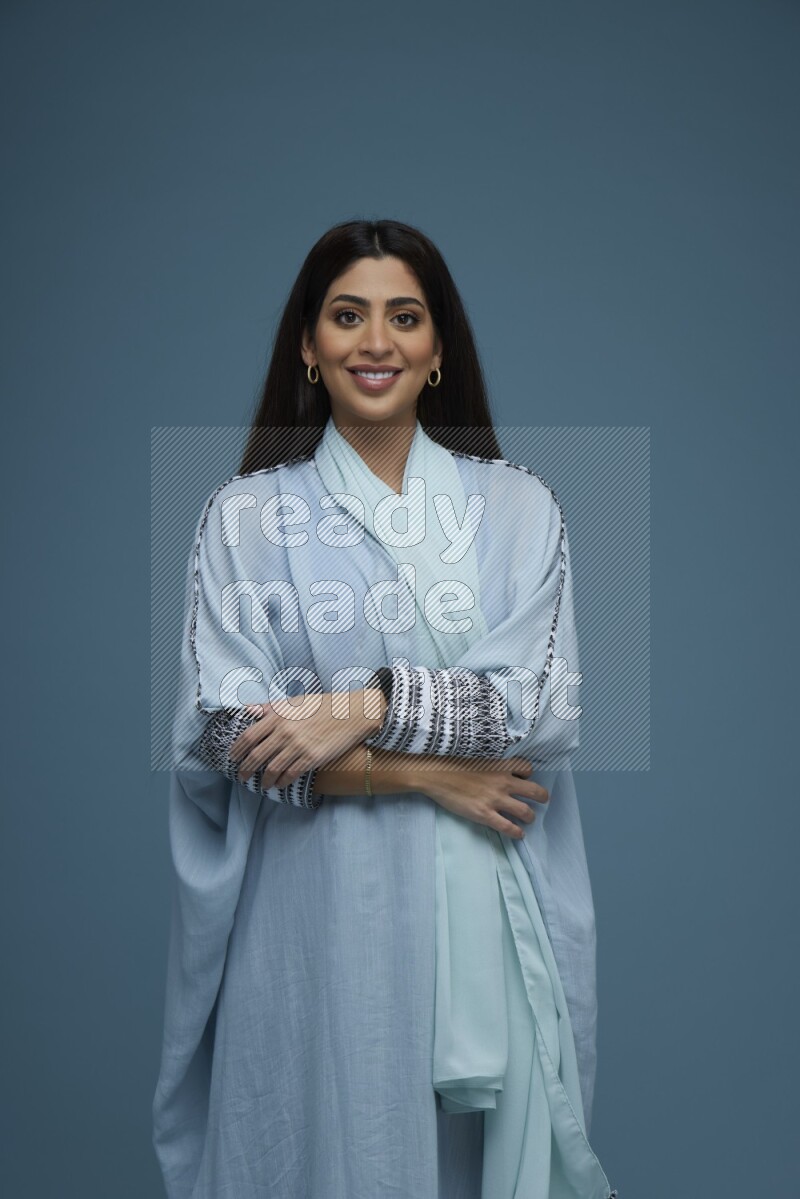 A woman posing in a blue background wearing blue Abaya no Hijab