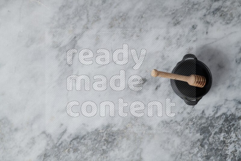 وعاء فخاري أسود مع ملعقة عسل خشبية بداخله على خلفية من الرخام الرمادي