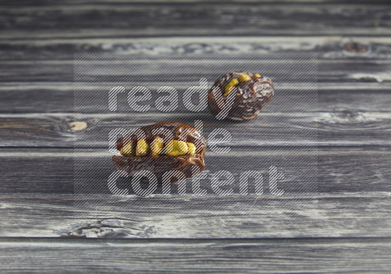 two pistachio stuffed madjoul dates on a wooden grey background