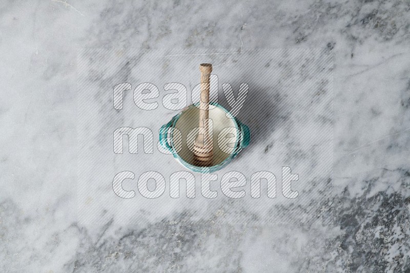 Multicolored Pottery Bowl with wooden honey handle in it, on grey marble flooring, Top View