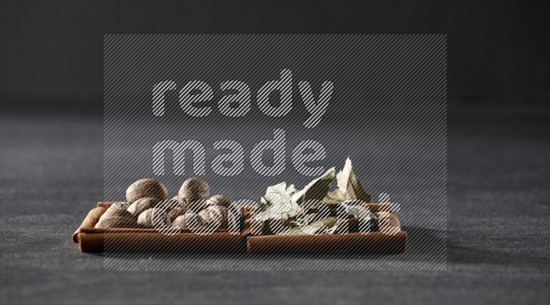 2 squares of cinnamon sticks full of nutmegs and bay laurel leaves on black flooring