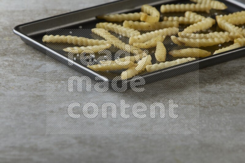 crinkle fries in a black stainless steel rectangle tray on grey textured counter top