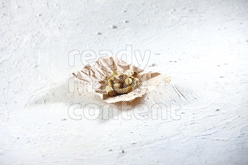 Dried turmeric whole fingers in a crumpled piece of paper on textured white flooring