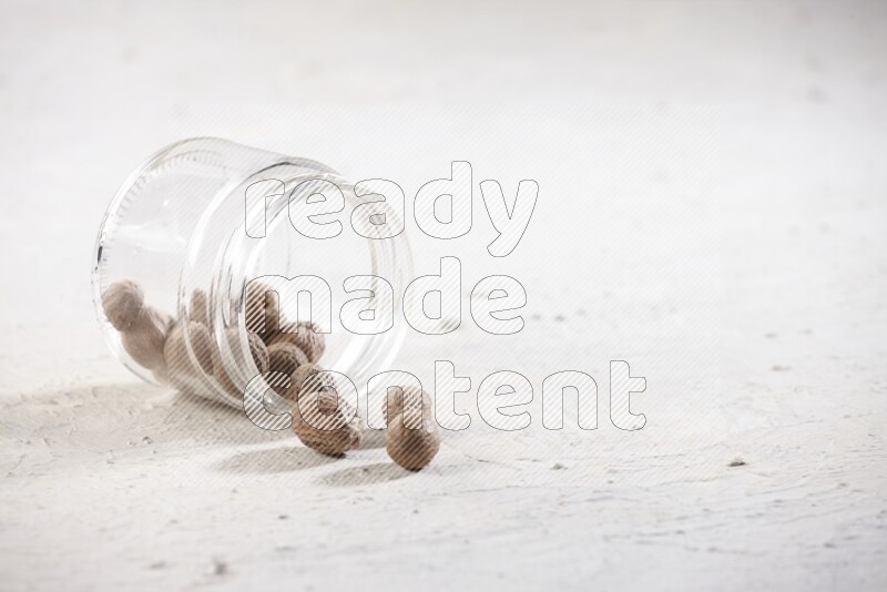 A glass jar full of nutmeg flipped and the seeds spread out on a textured white flooring