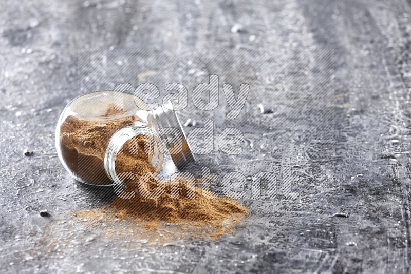 Flipped herbal glass jar full of cinnamon powder on textured black background