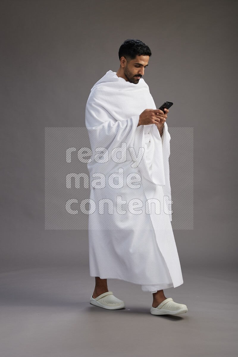 A man wearing Ehram Standing texting on phone on gray background