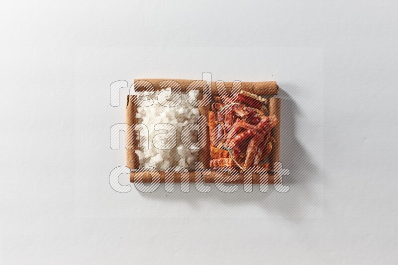 مربعان من أعواد القرفة ممتلئان بالفلفل الحار المجفف والملح الأبيض علي خلفية بيضاء