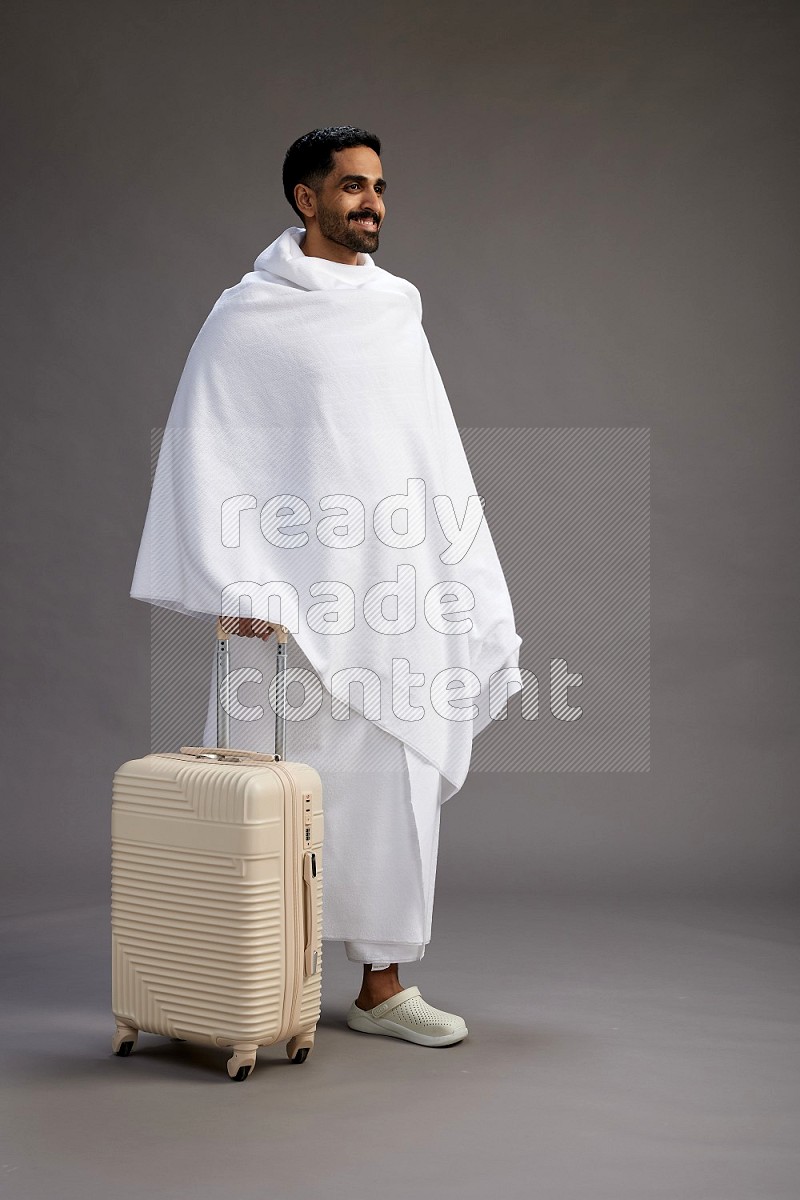 A man wearing Ehram Standing holding traveling bag on gray background