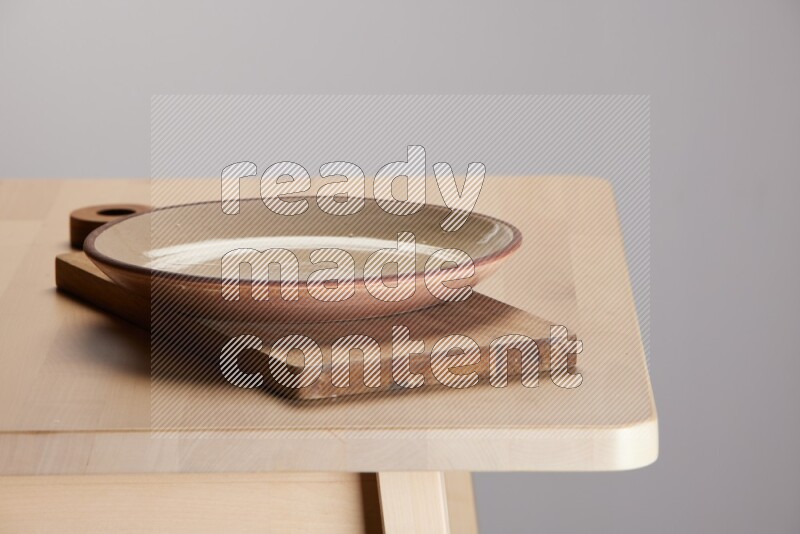 multi-colored pottery Plate placed on a  wooden rectangular cutting board on the edge of wooden table