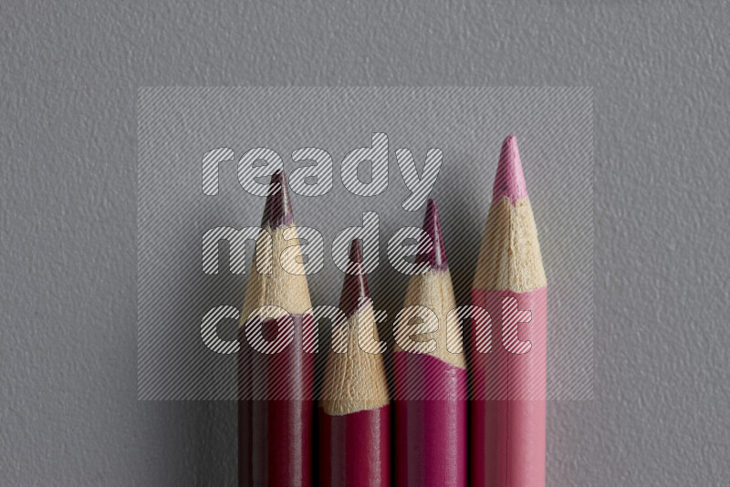 A collection of sharpened colored pencils arranged showcasing a gradient of pink hues on grey background