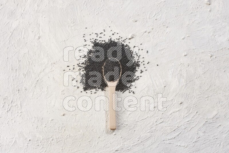 A wooden spoon full of black seeds on textured white flooring