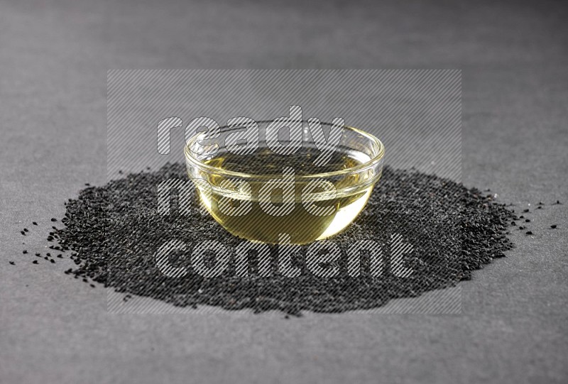 وعاء زجاجي ممتلئ بزيت حبة البركة محاط ببذور حبة البركة على أرضية سوداء