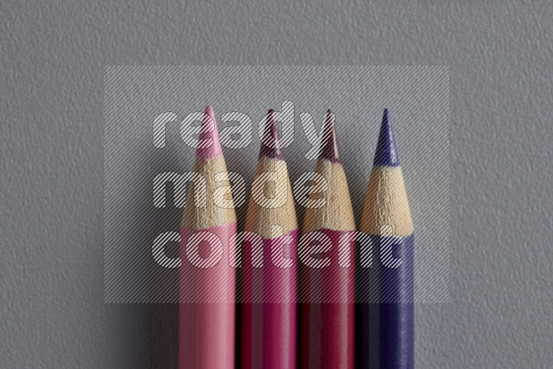 A collection of sharpened colored pencils arranged showcasing a gradient of pink and purple hues on grey background
