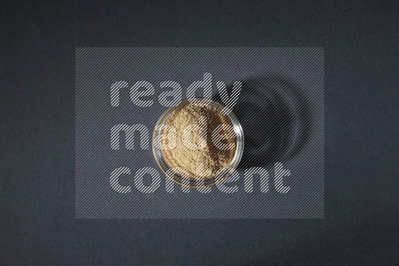 وعاء زجاجي ممتلئ ببودرة الكمون على خلفية سوداء