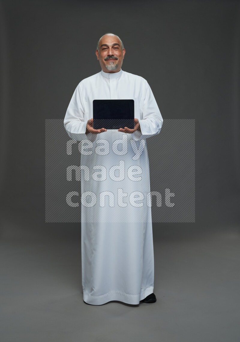 Saudi man without shomag Standing working on tablet on gray background