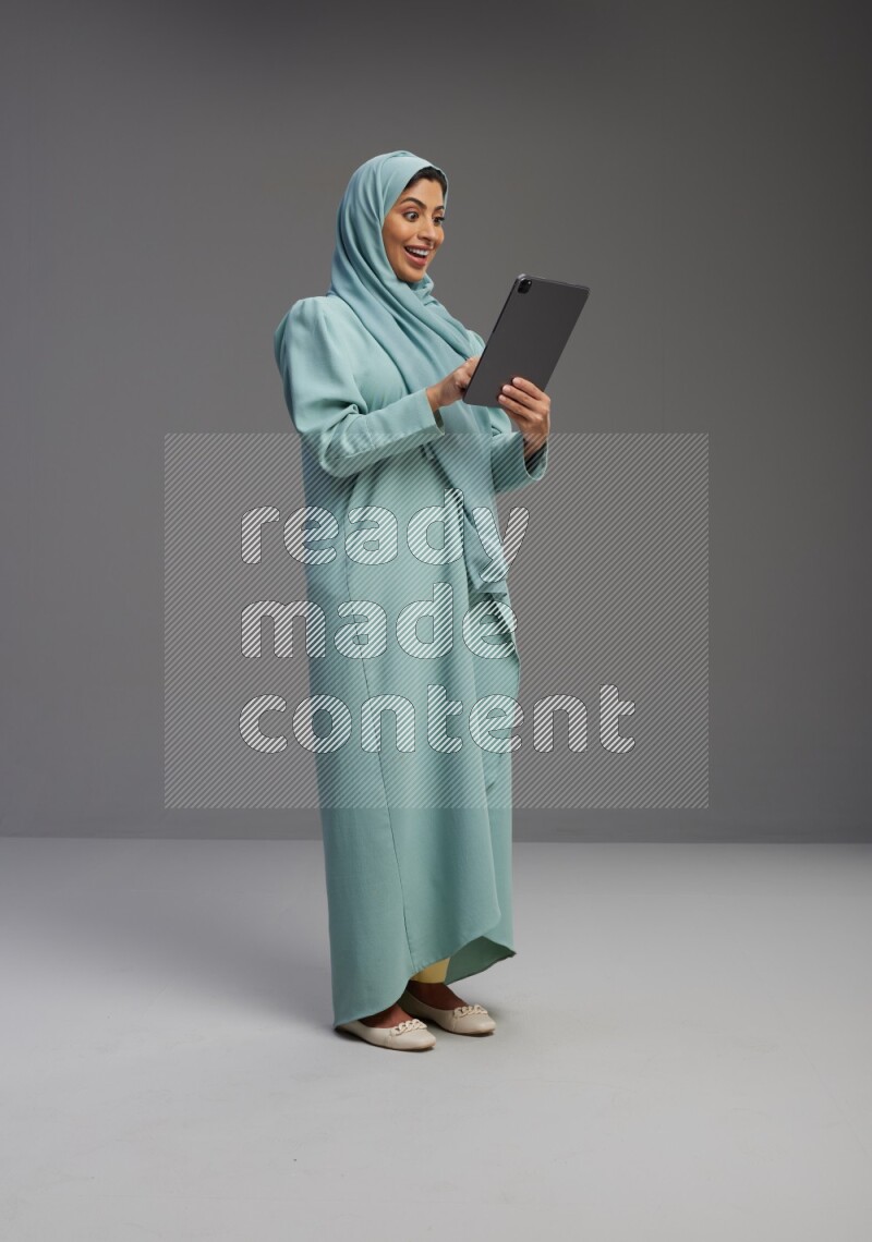 Saudi Woman wearing Abaya standing working on tablet on Gray background