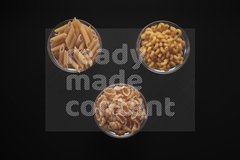 Different pasta types in glass bowls on black background