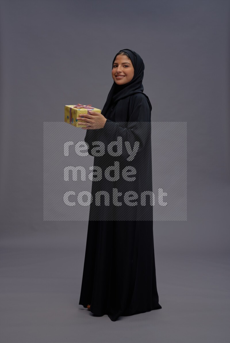 Saudi woman wearing Abaya standing holding gift box on gray background
