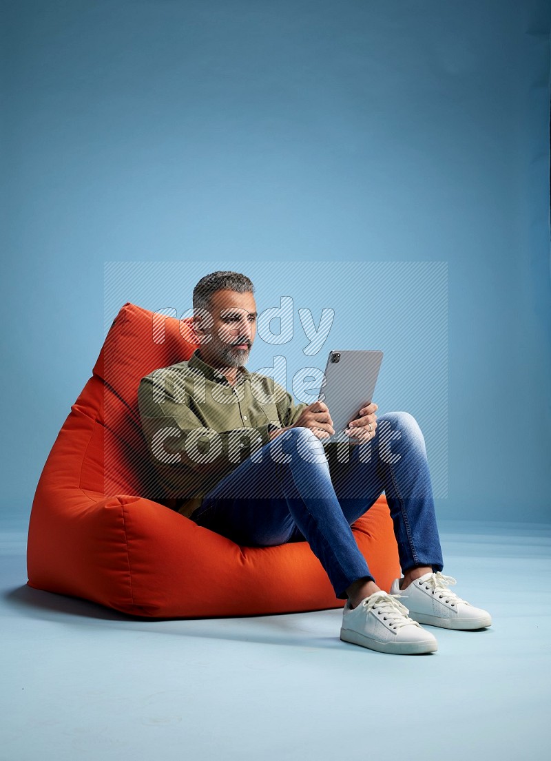 A man sitting on an orange beanbag and working on tablet