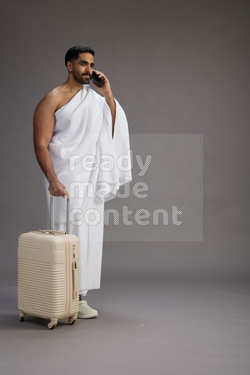 A man wearing Ehram Standing holding traveling bag on gray background