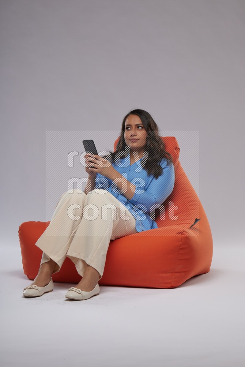 A woman sitting on an orange beanbag and texting on phone