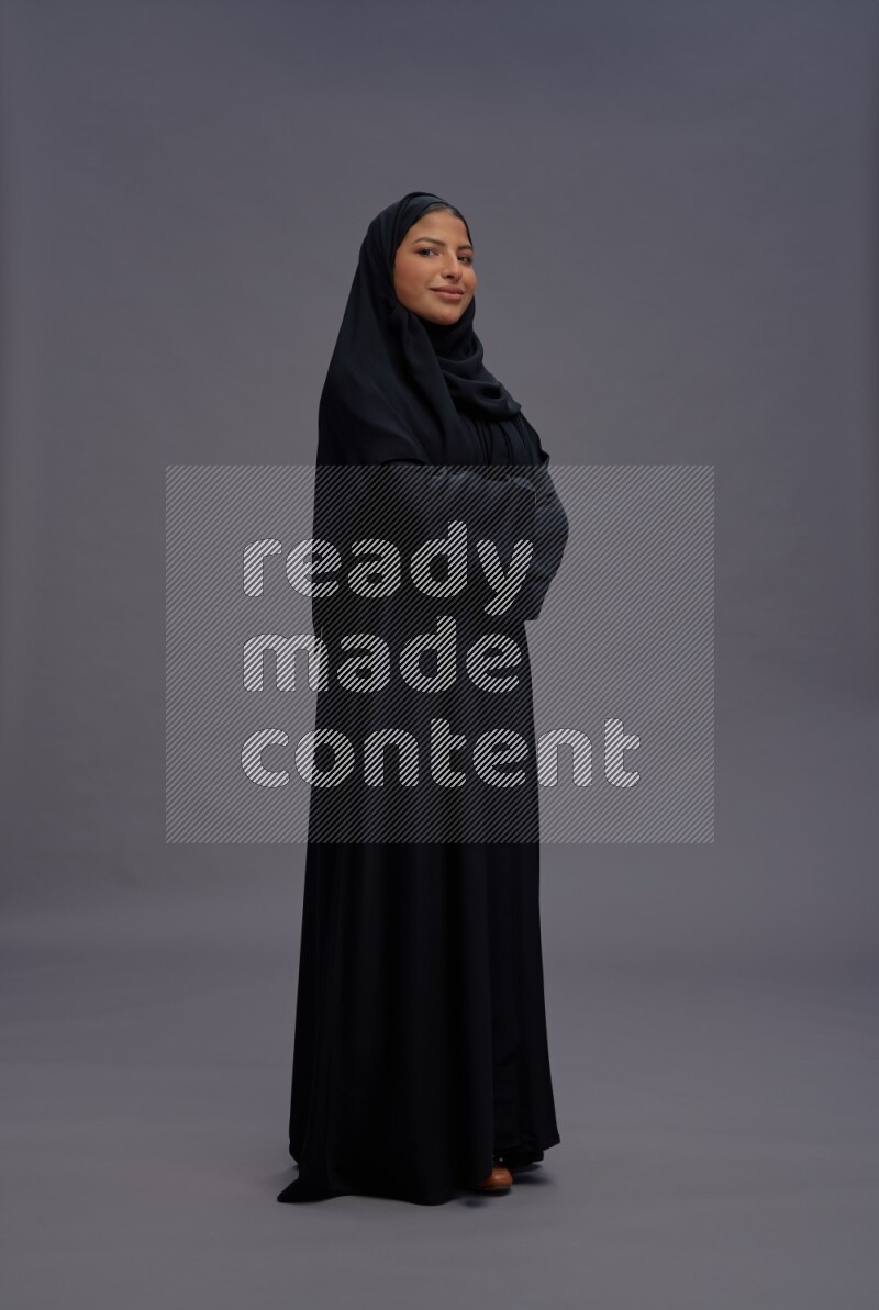 Saudi woman wearing Abaya standing with crossed arms on gray background