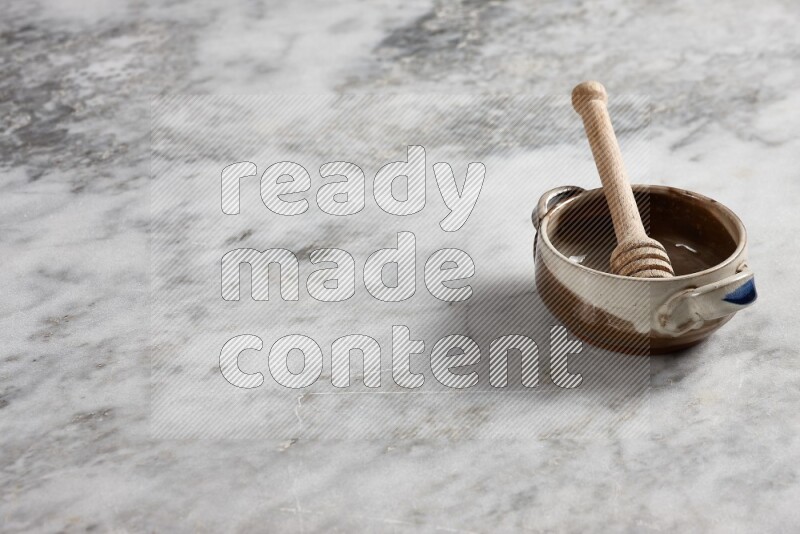 Multicolored pottery bowl with wooden honey dipper in it on grey marble background