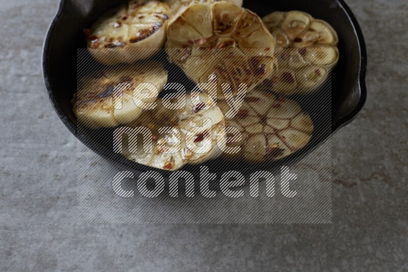 half's roasted garlic in a black pan on a grey textured countertop