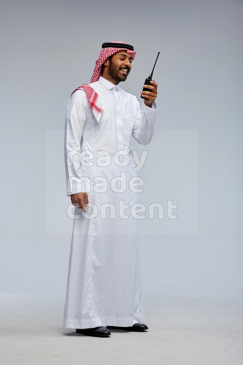 Saudi man Wearing Thob and shomag standing holding walkie-talkie on Gray background
