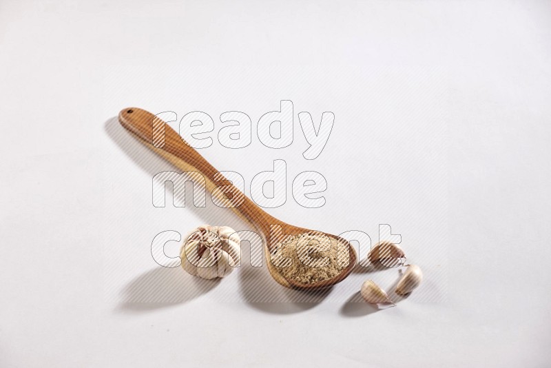 A wooden ladle full of garlic powder and beside it garlic bulb and cloves on a white flooring in different angles